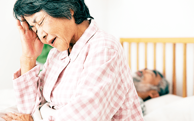 睡眠不足で頭をかかえるシニア女性